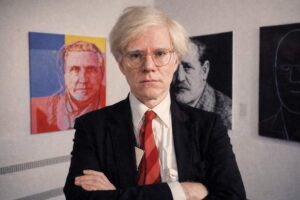 Andy Warhol: Porträtfoto silber-weißen Perücke, Brille und roter Krawatte vor seinen Kunstwerken