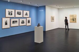 Kollwitz Museum Köln - Ausstellung "Die Folge Krieg" : Blaue Wand mit gerahmten Grafiken und Plakat mit der Aufschrift "Nie wieder Krieg"