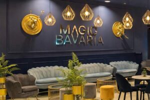 Magic Bavaria Erlebnismuseum - München - Loungebereich mit blauen Samtsofas, goldenen Hirschköpfen und moderner Beleuchtung