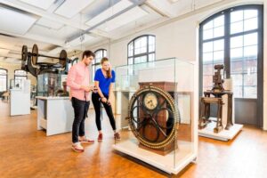 Museum der Arbeit - Hamburg - Arbeiterkontrolluhr: Besucher betrachten eine historische Kontrolluhr aus dem Industriezeitalter