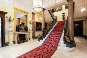 The Wallace Collection - London - Eingangshalle: Die prachtvolle Eingangshalle mit einer Marmortreppe, einem roten Teppichläufer, goldenen Geländern und antiken Büsten