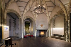 Tower of London - Mittelalterlicher Palast: Ein historischer Saal mit Steingewölbe, einem Thronsessel unter einem Baldachin und einem brennenden Kamin
